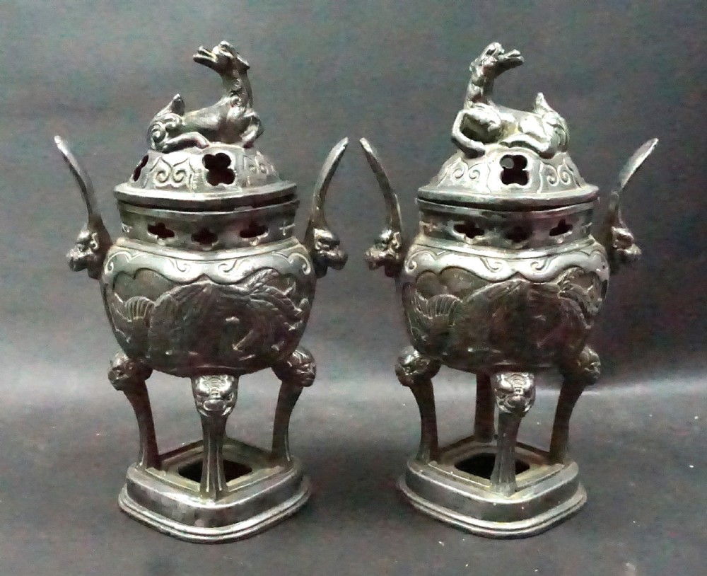 A pair of late Qing Dynasty Chinese antimony metal censers featuring relief dragon panels, animal finials, and pierced lids.