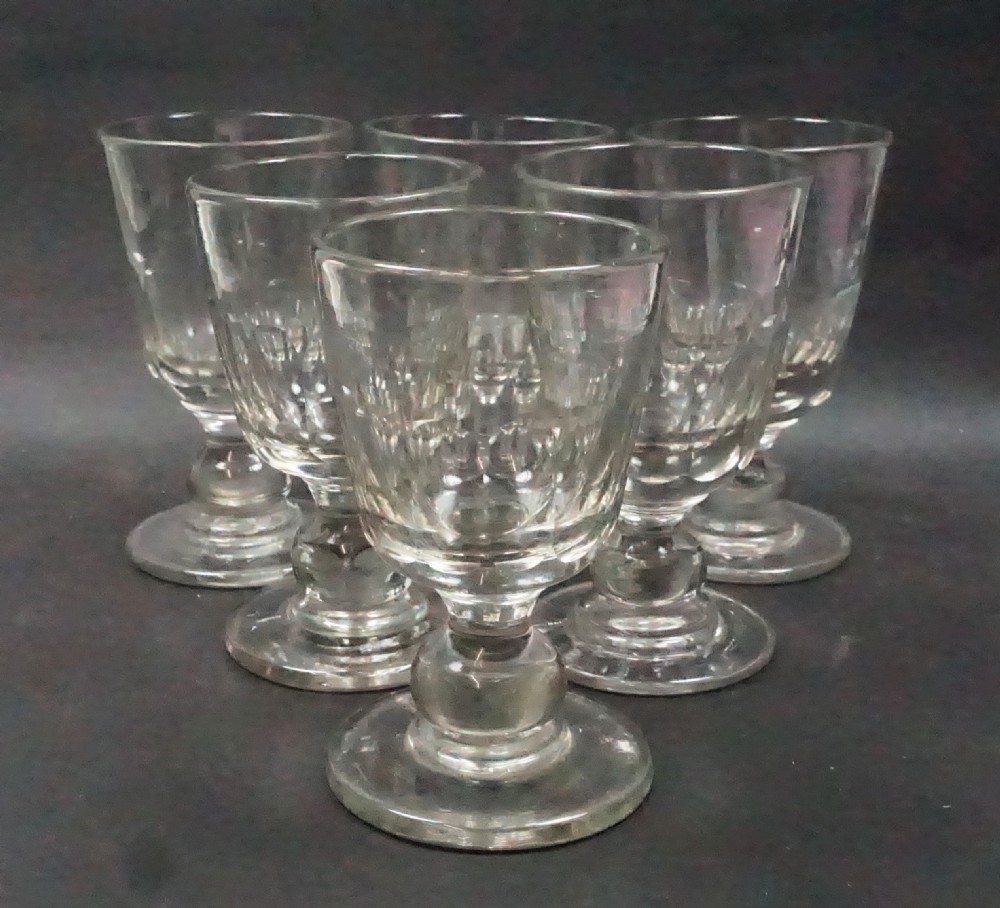 A set of six clear cut-crystal glass rummers with rounded bowls, baluster stems, and wide circular feet arranged in a group.