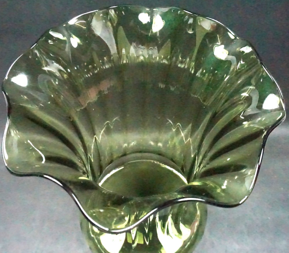 An olive green optically blown glass vase with a wavy flared rim, vertical ribbed texture, and a wide circular base. View II