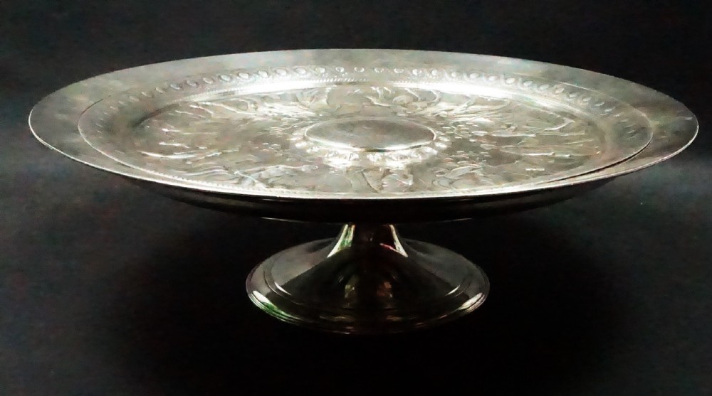 A circular Victorian silver-plated bronze tazza featuring detailed classical relief artwork depicting mythological figures surrounding a central raised boss. View II