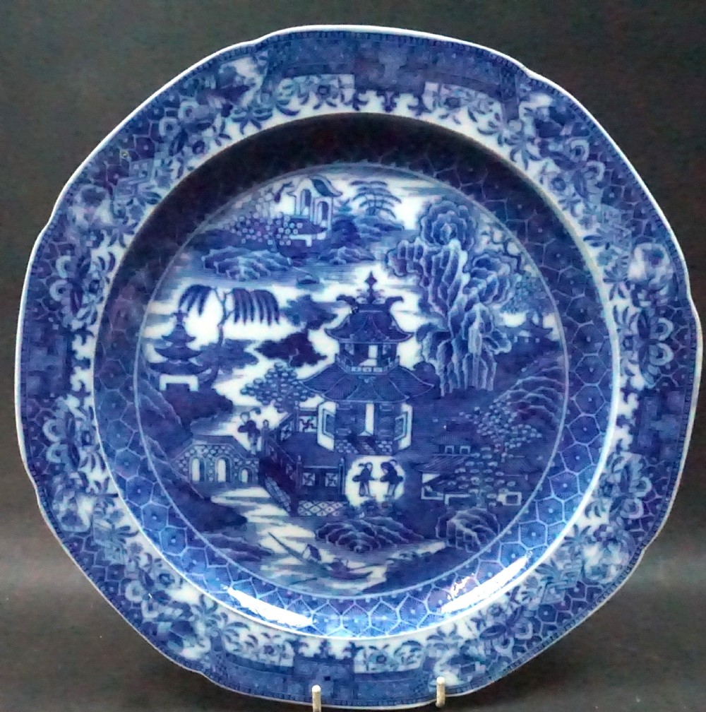 A circular 18th-century Caughley blue and white pearlware charger featuring a detailed Willow pattern chinoiserie landscape motif.