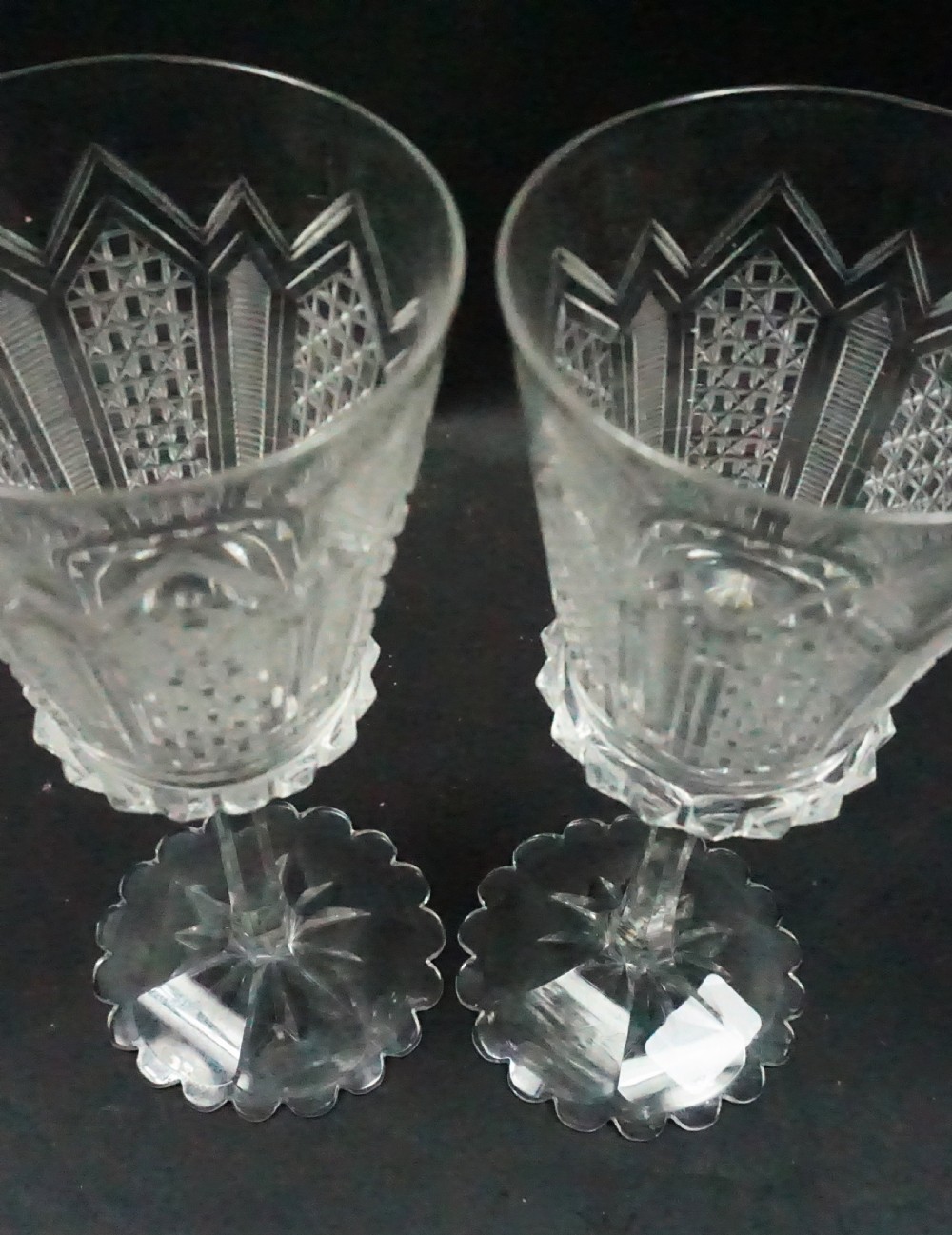 A pair of mid-Victorian clear cut crystal wine glasses featuring geometric cut bowls, faceted stems, and star-cut scalloped foot bases. View II