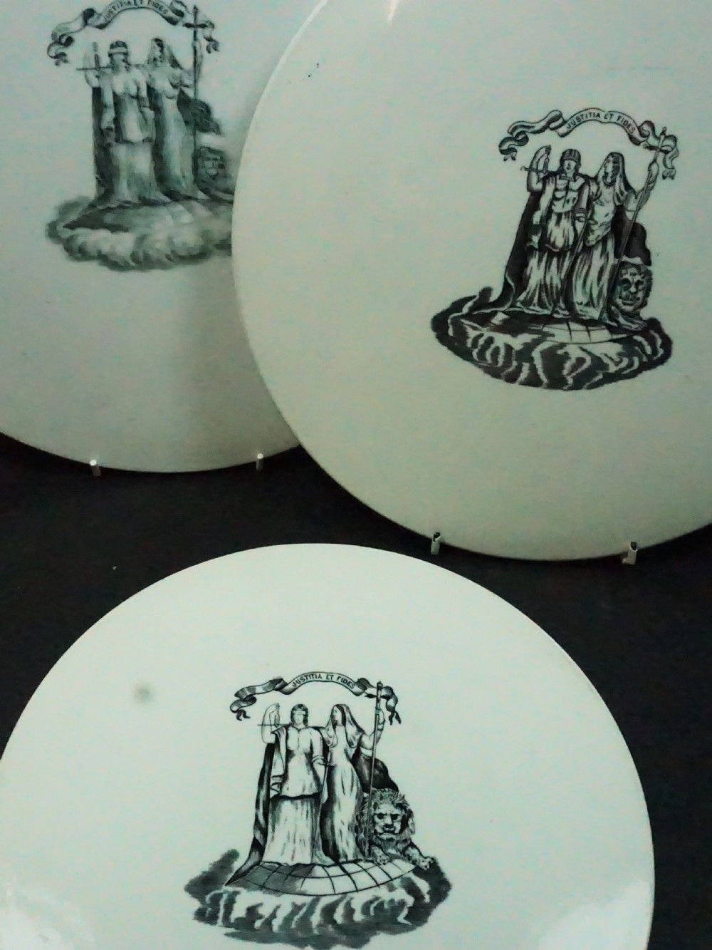 Three circular white ceramic scale pans of varying sizes featuring black transfer-printed justice emblems on their surfaces. View II