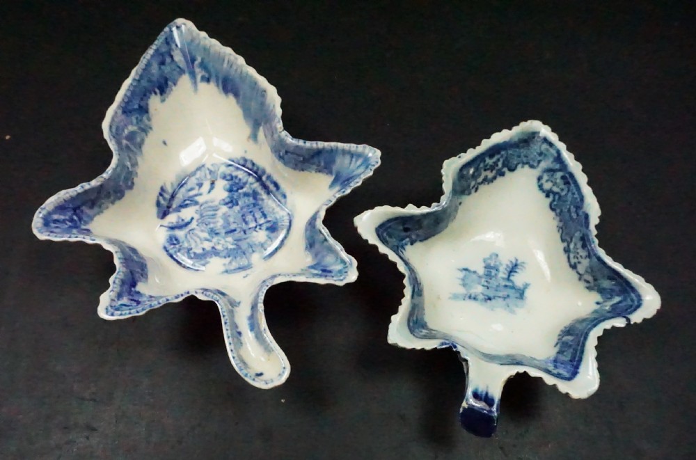 A pair of early nineteenth-century leaf-shaped ceramic pickle dishes featuring blue transfer-printed landscape patterns and molded stem handles.