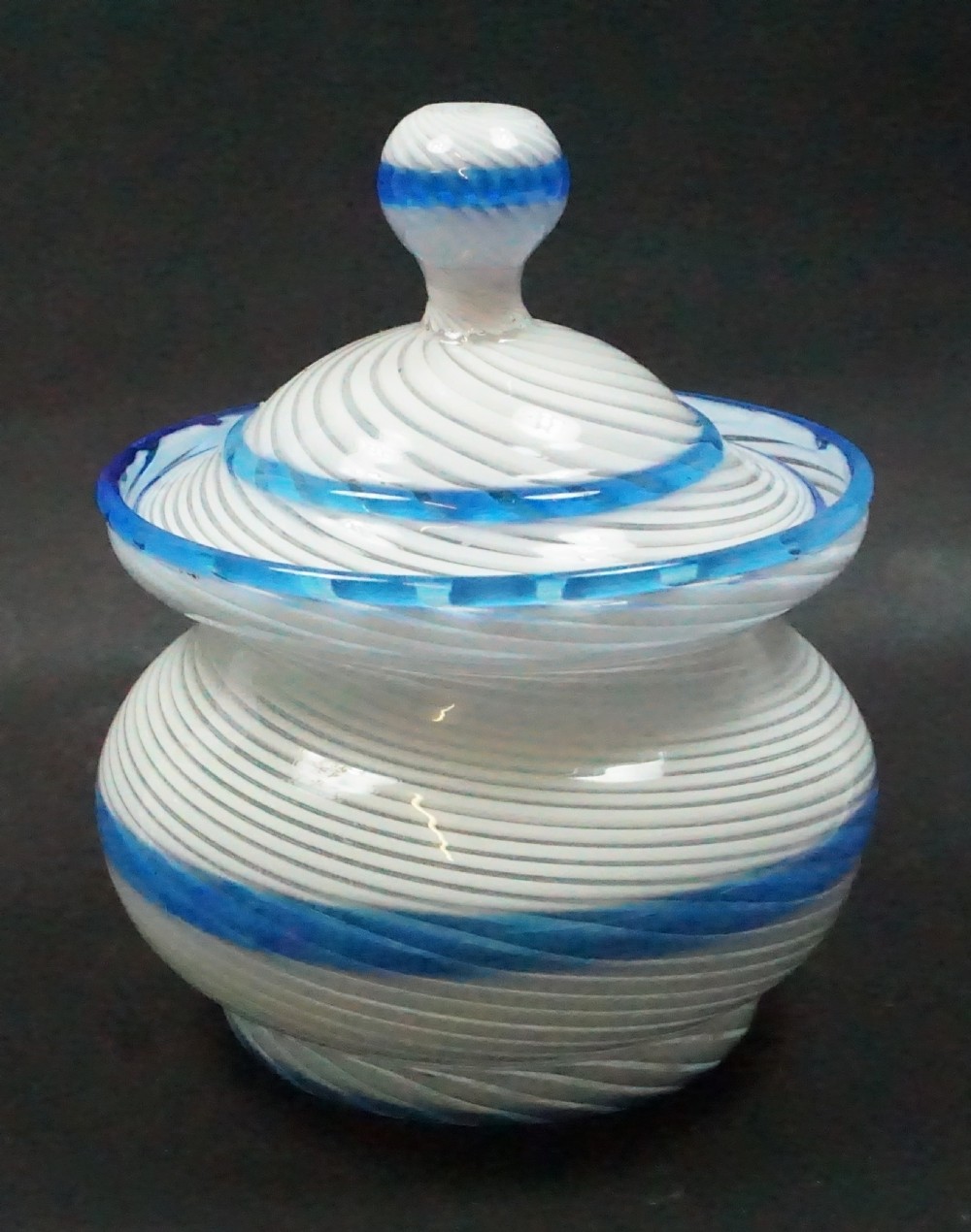 A 19th-century lidded glass sugar bowl crafted with spiralling white latticinio strands and trimmed with cobalt blue cane rims.