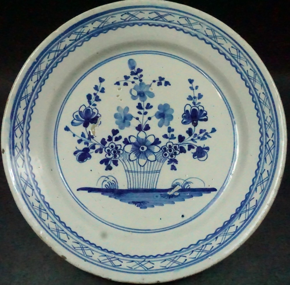 An 18th-century Dutch Delftware tin-glazed earthenware plate decorated with cobalt blue hand-painted floral motifs in a central basket.