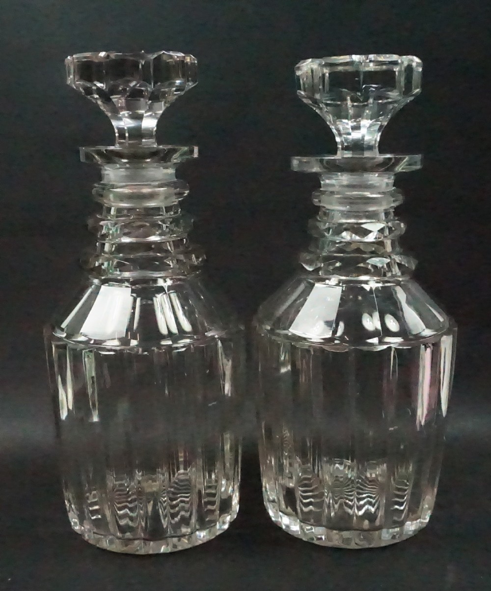 A pair of antique Regency clear cut crystal decanters featuring neck rings, vertical pillar cut bodies, and faceted stoppers.