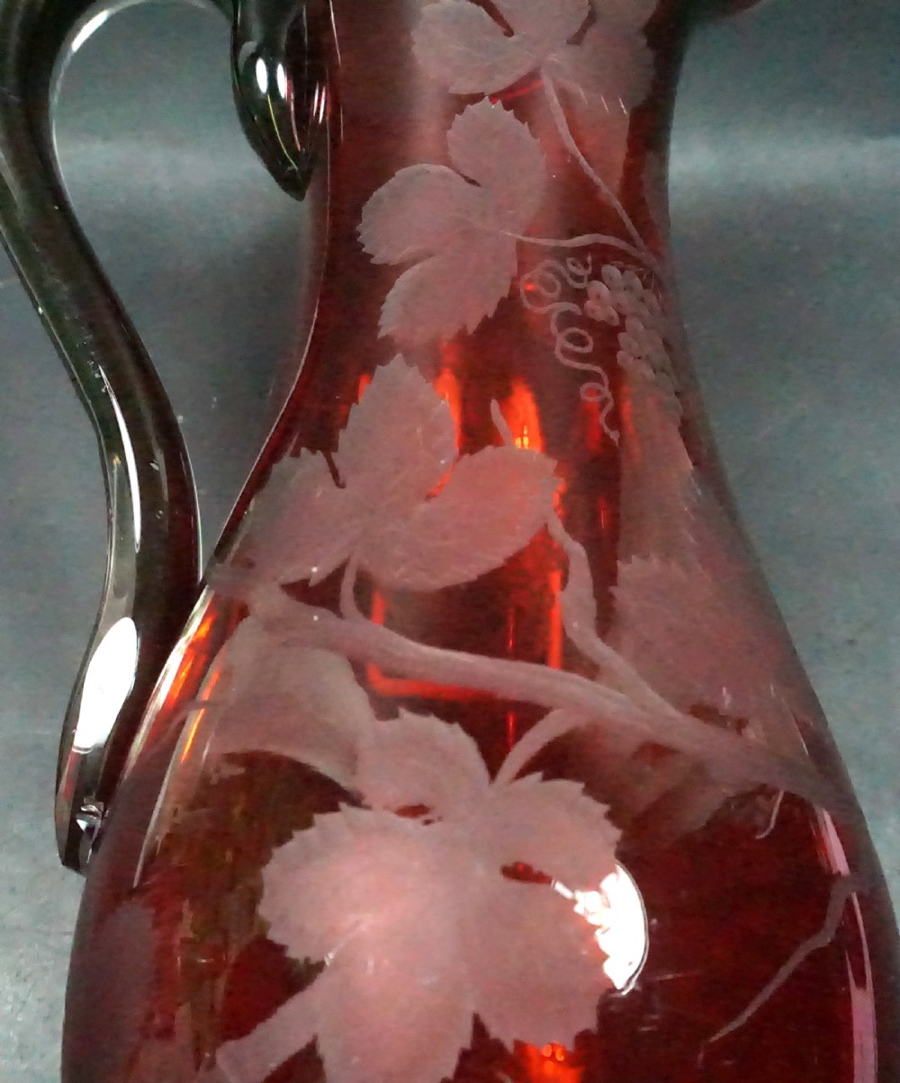 A Victorian ruby red glass jug with a dark applied handle and wheel-engraved fruiting vine patterns across the body. View II