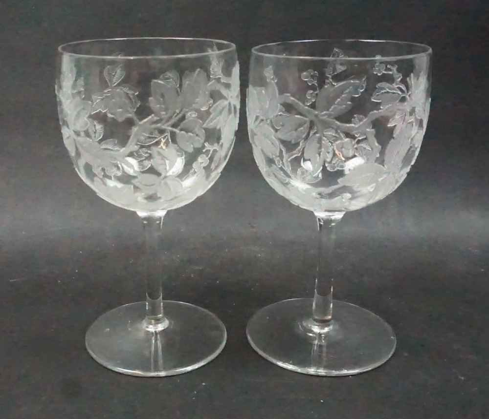 A pair of clear glass stemmed goblets featuring raised acid-etched relief carvings of foliage and fruit on the bowls.
