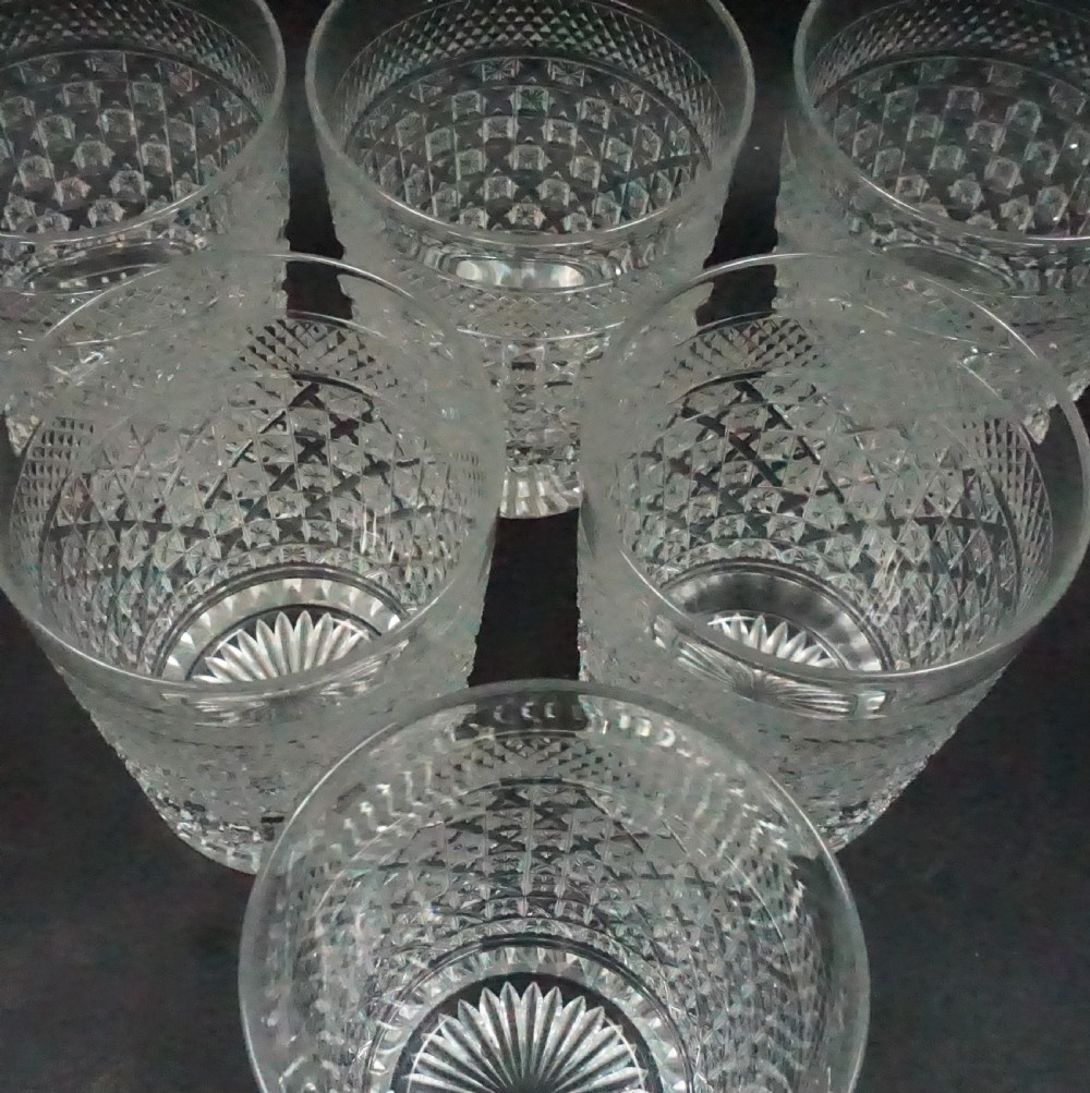 A set of six clear cut crystal whisky tumblers featuring geometric diamond facet cuts and a starburst base pattern arranged on a dark background. View II