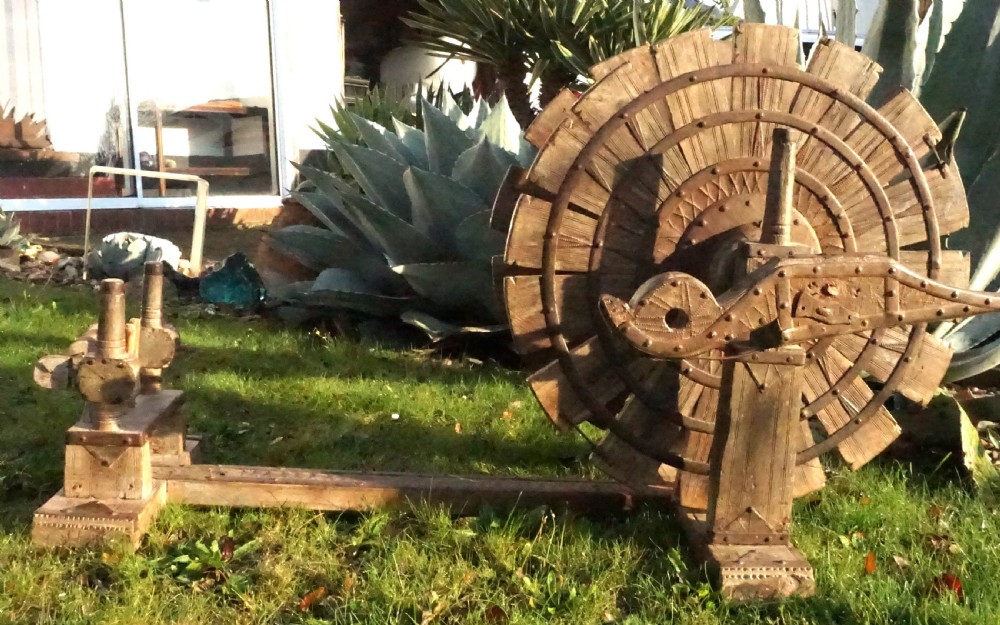 An early twentieth-century Indian oak charkha spinning wheel featuring a slatted drive wheel reinforced with iron bands on a low wooden base.