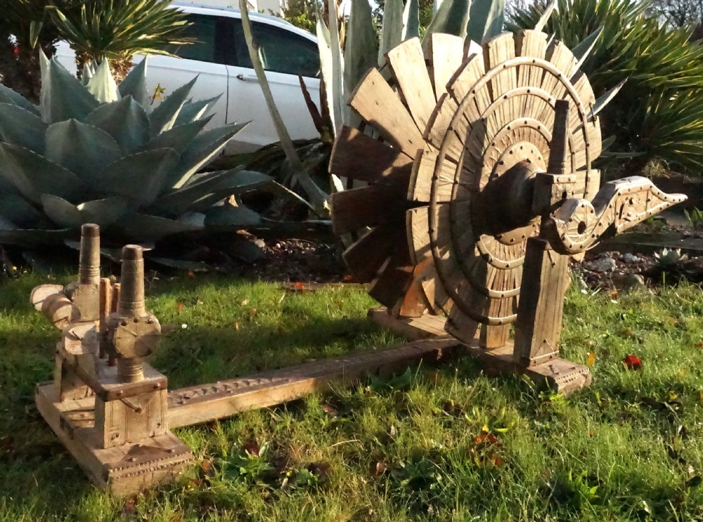 An early twentieth-century Indian oak charkha spinning wheel featuring a slatted drive wheel reinforced with iron bands on a low wooden base. View II
