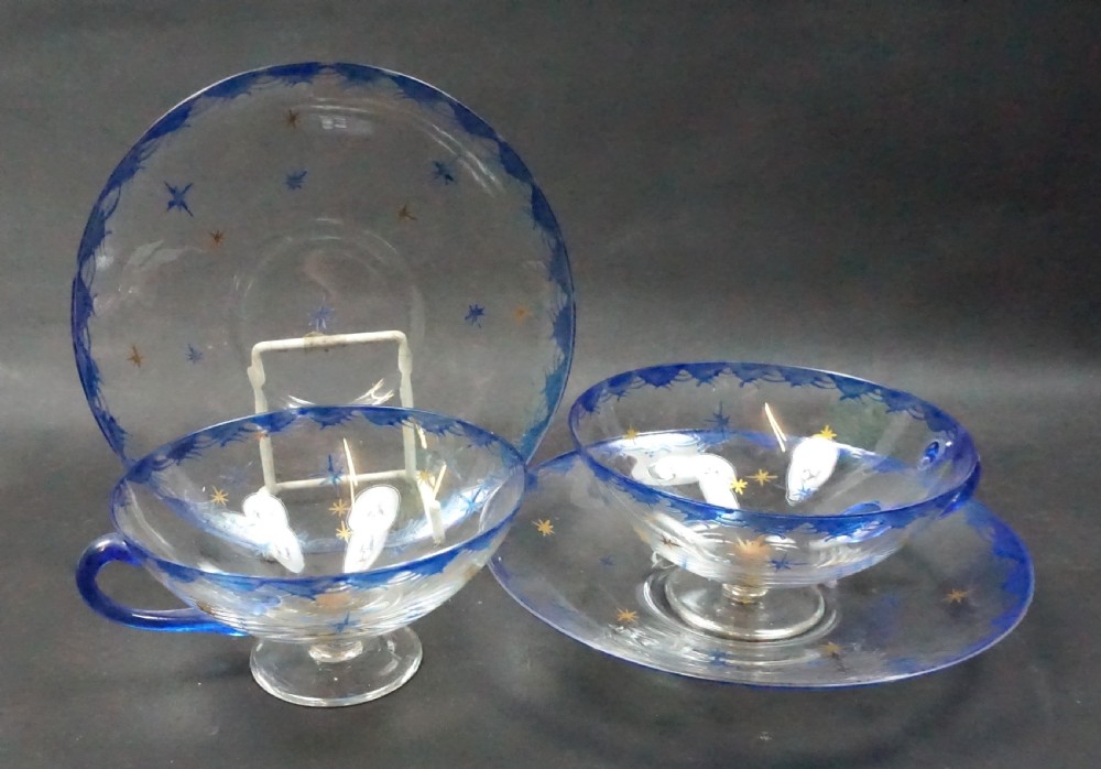 Pair of clear glass teacups and matching saucers featuring cobalt blue rim borders and painted gold star motifs.