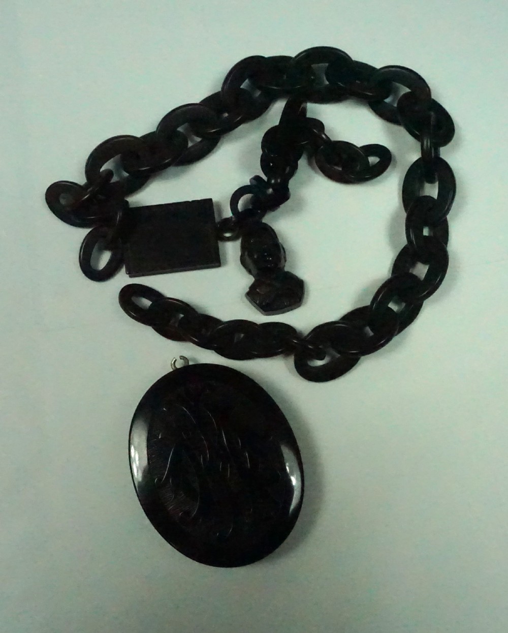 A Victorian black carved jet oval locket attached to a linked Albert chain section featuring two small carved charms.