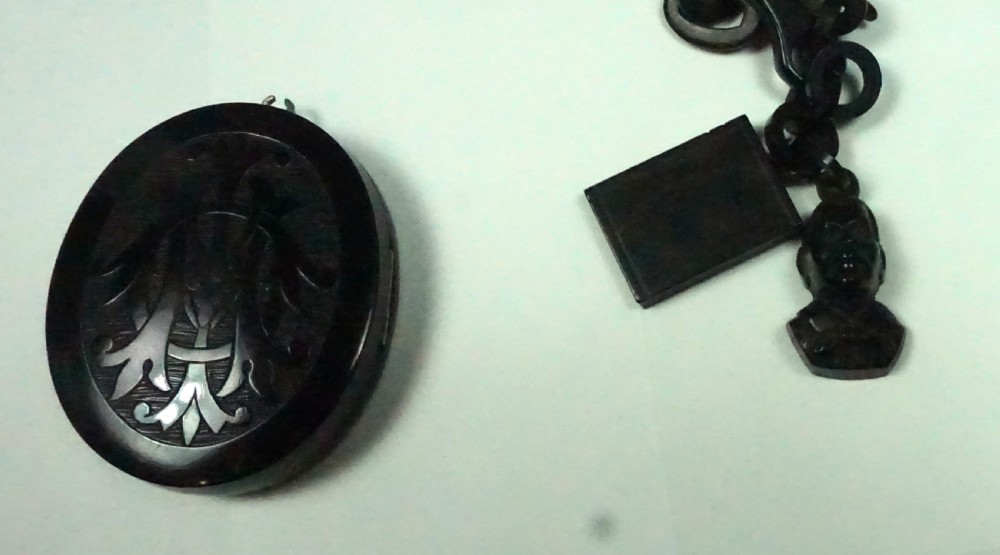 A Victorian black carved jet oval locket attached to a linked Albert chain section featuring two small carved charms. View III