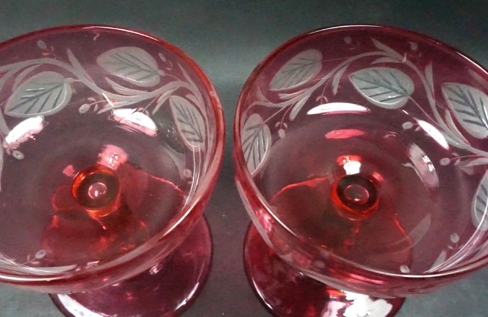 A pair of Victorian cranberry glass champagne coupes featuring hand-engraved convolvulus leaves and vines over clear crystal stems. View II