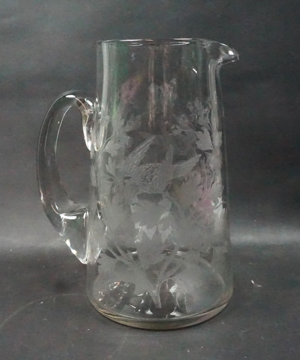 A late Victorian clear glass lemonade jug featuring hand-etched decorations of birds perched among leafy foliage with an applied glass handle.