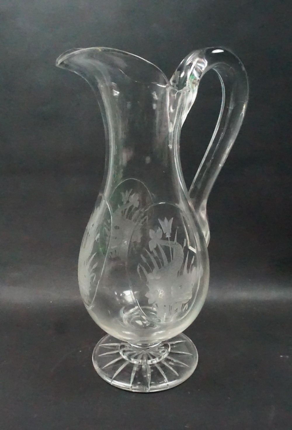 Clear Victorian lead crystal champagne jug featuring etched dolphin motifs and a star-cut footed base.