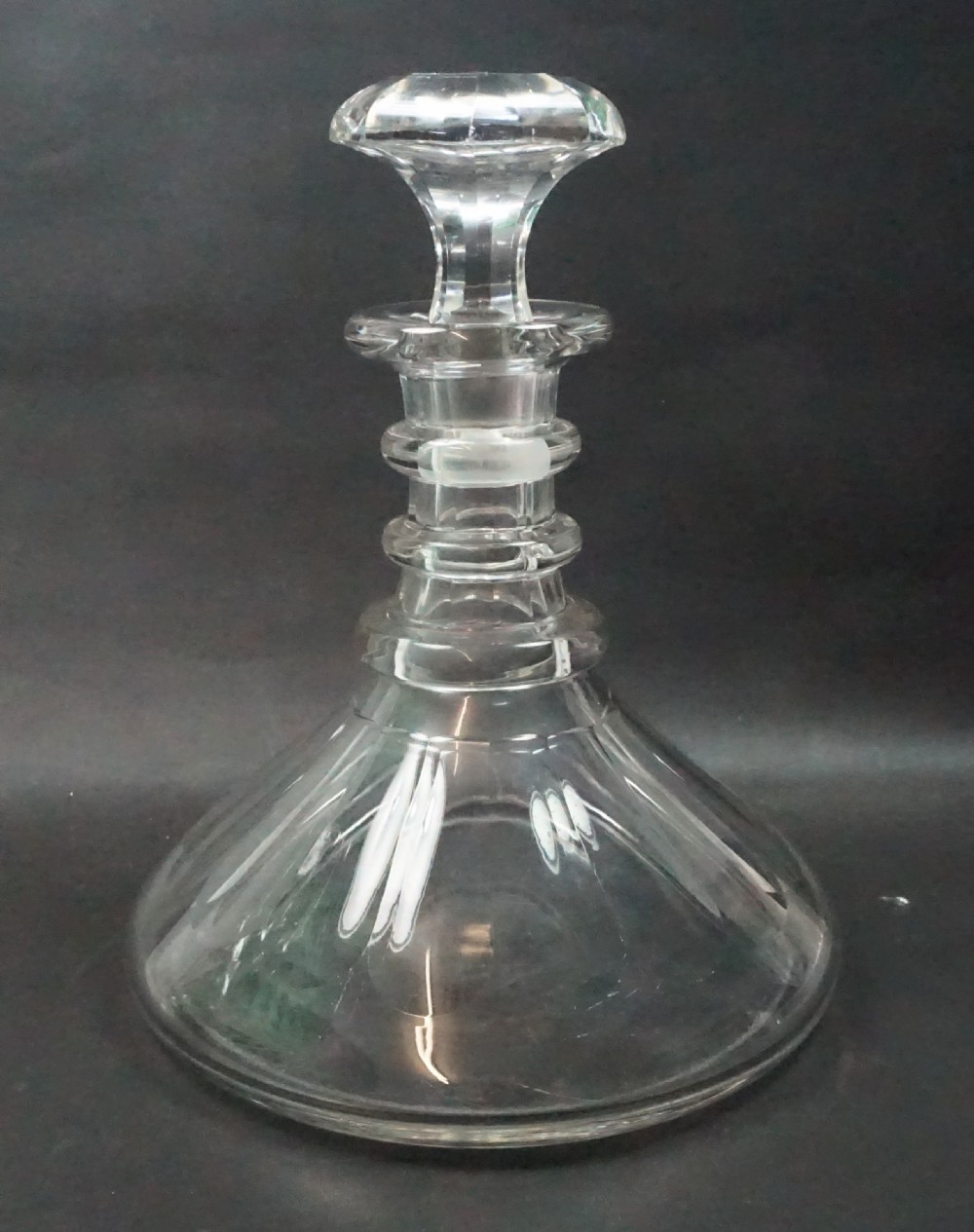 A Regency period clear lead crystal ships decanter featuring a wide conical base, triple ring neck, and flat cut stopper.