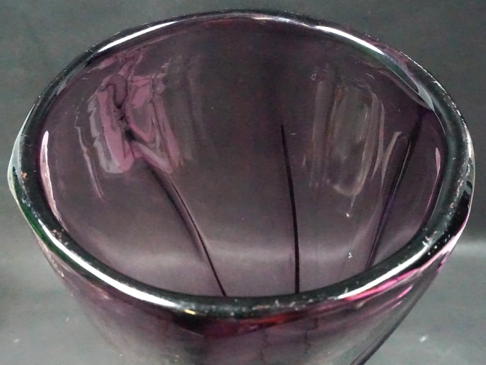 A tall heavy amethyst purple glass vase with a twisted fluted body resting on a thick rounded dark glass base. View II