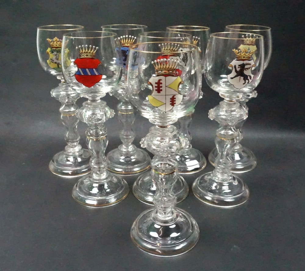A group of eight clear glass roemer goblets decorated with colourful enamelled heraldic shields and gilded rims on knopped stems.