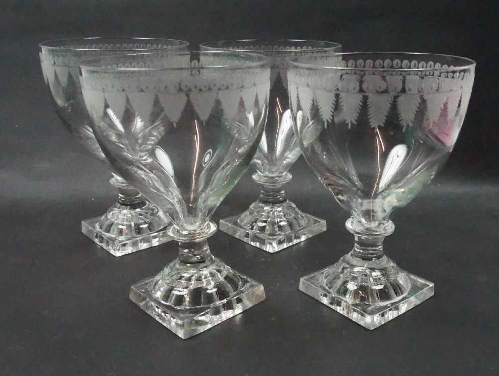 A set of four clear antique crystal glass rummers featuring wheel-engraved bowls and square lemon squeezer moulded bases.