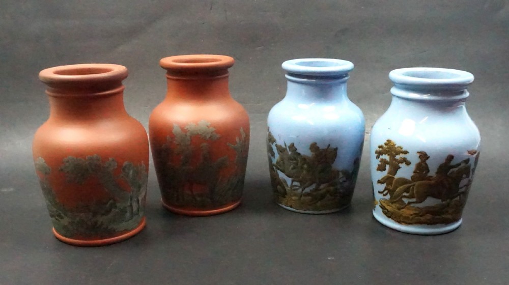 Four small Victorian ceramic paste jars, two in unglazed terracotta and two in light blue glaze, featuring dark transfer-printed equestrian scenes around their body.