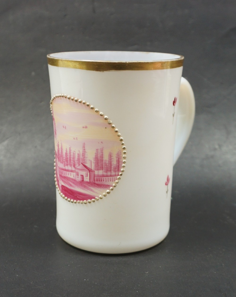 An opaque white opaline glass tankard featuring a hand-painted oval landscape vignette framed by raised gold beaded dots and a gilded rim.