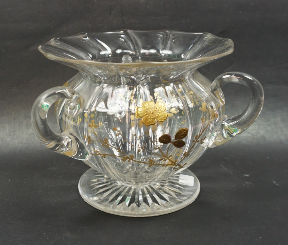 A clear cut crystal bowl featuring three applied handles, a flared scalloped rim, and gilt floral paste decoration around the body.
