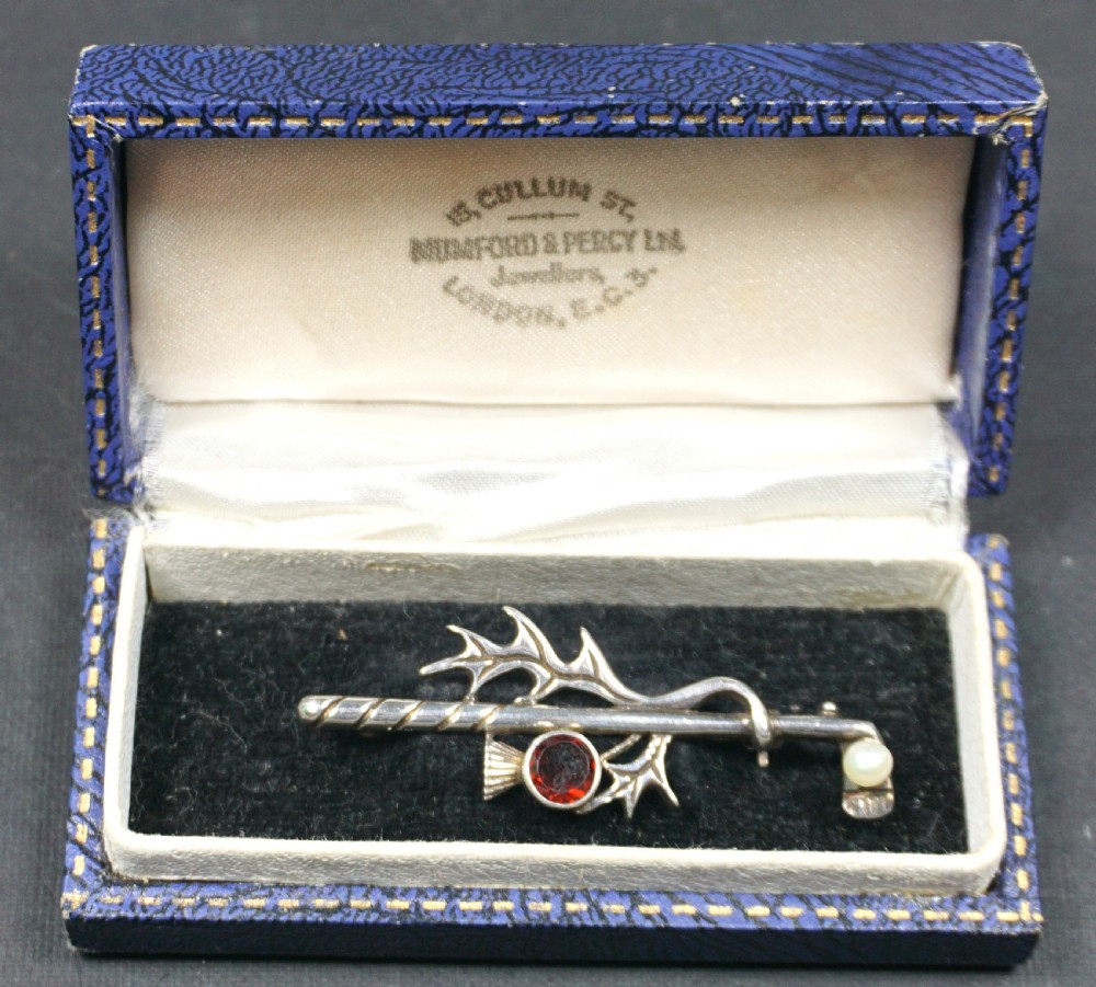 An Edwardian silver brooch shaped as a golf club with a pearl ball and a Scottish thistle motif holding a circular red stone, inside a fitted blue presentation box.