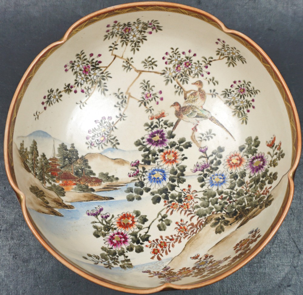 A Japanese ceramic Satsuma bowl with a lobed rim, decorated with hand-painted birds, flowers, and a landscape scene on a cream crackle-glazed interior.