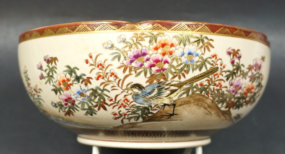 A Japanese ceramic Satsuma bowl with a lobed rim, decorated with hand-painted birds, flowers, and a landscape scene on a cream crackle-glazed interior. View II