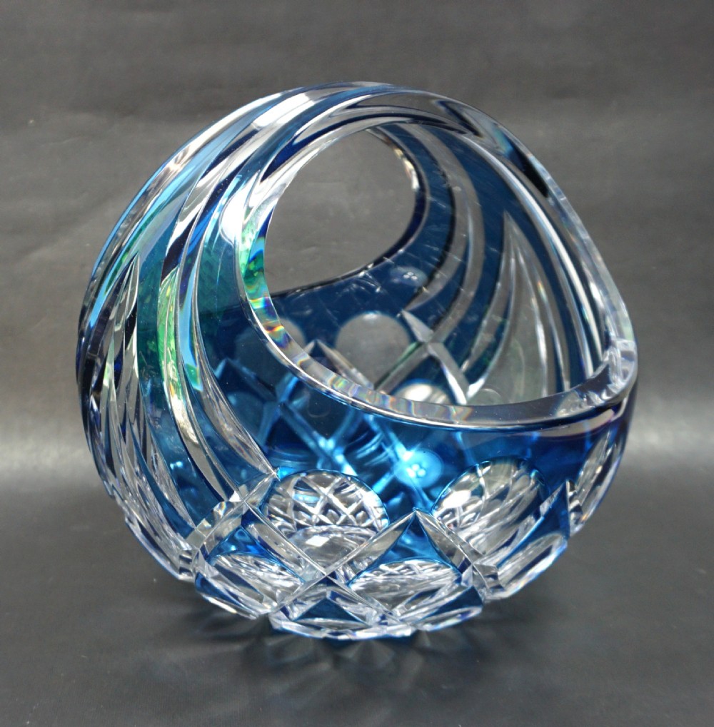A circular cobalt blue and clear cut crystal glass basket featuring an integrated arched handle and geometric faceting.