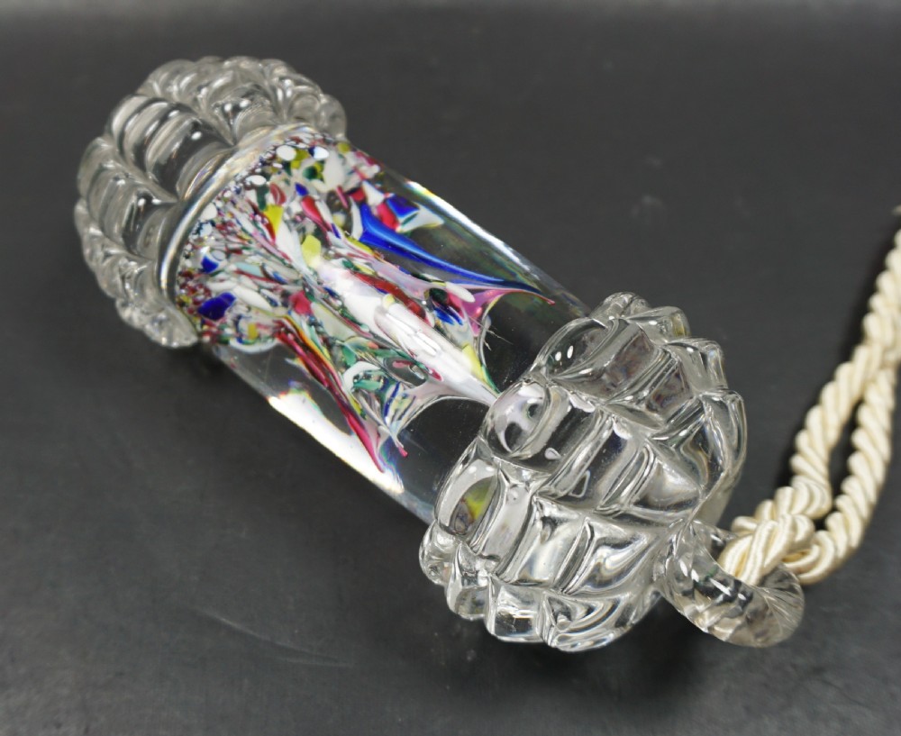 A cylindrical Victorian clear glass bell pull featuring internal multicoloured glass spatter inclusions, moulded faceted end caps, and a suspended twisted rope cord. View II