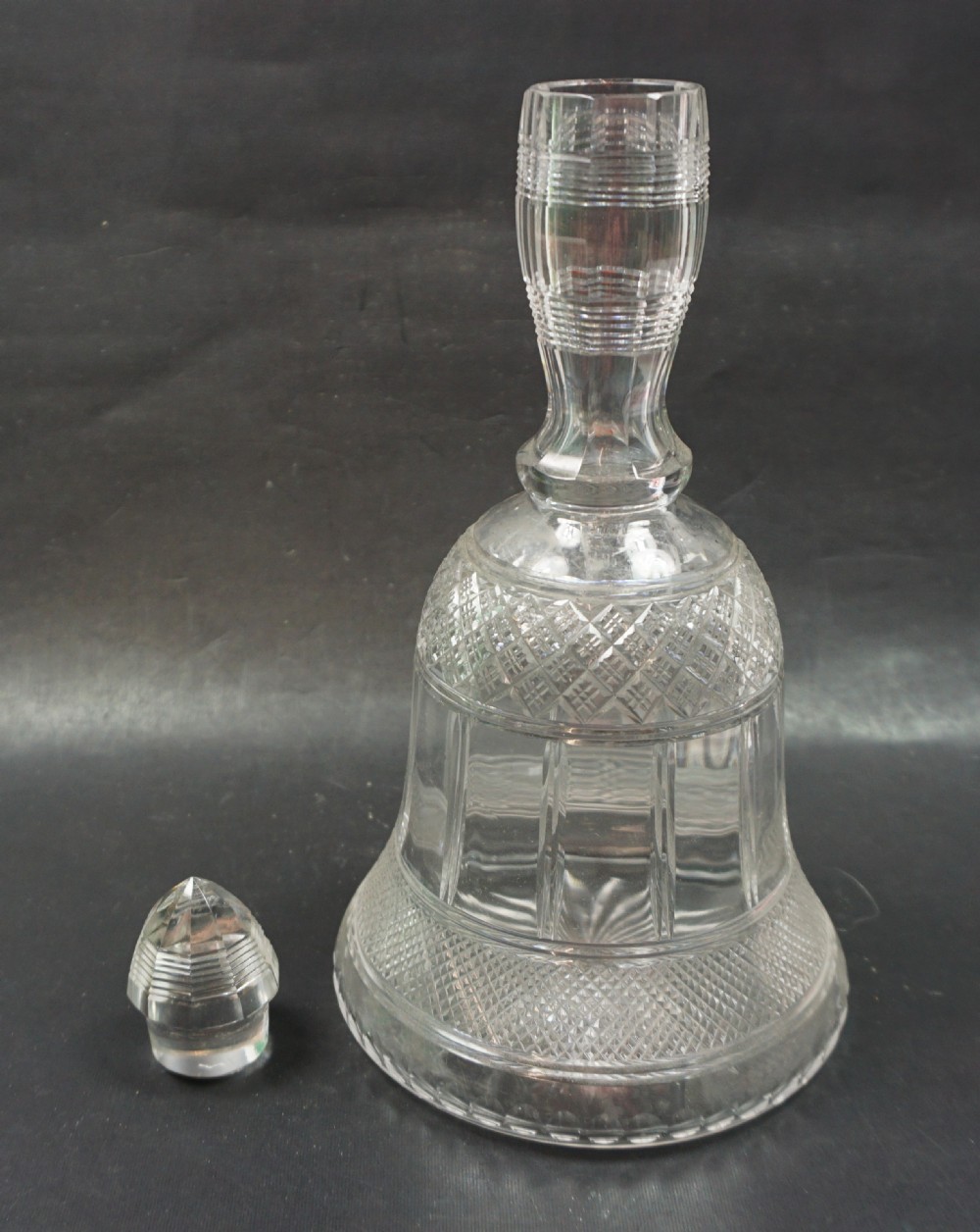 A clear cut crystal glass decanter shaped like a bell, featuring geometric cross-hatch and panel cut details with a matching pointed glass stopper. View II