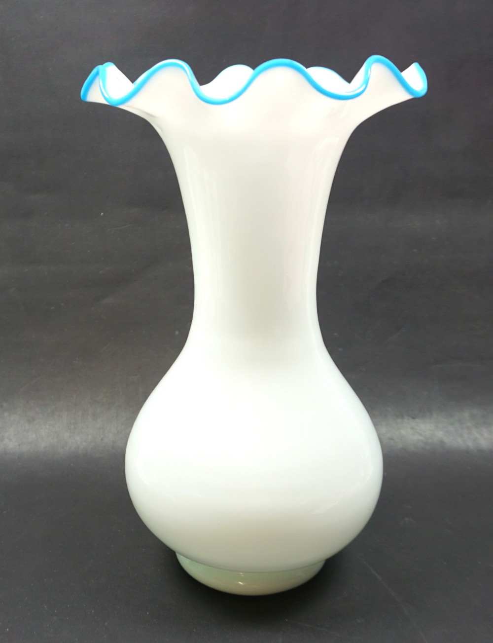 A white opaline glass vase featuring a bulbous base, flared neck, and a ruffled pale blue glass rim.