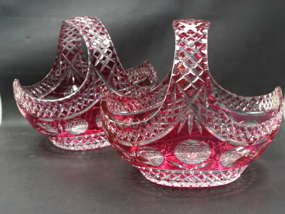 A pair of Art Deco ruby red cut-to-clear lead crystal glass baskets featuring geometric diamond facets and curved handles.