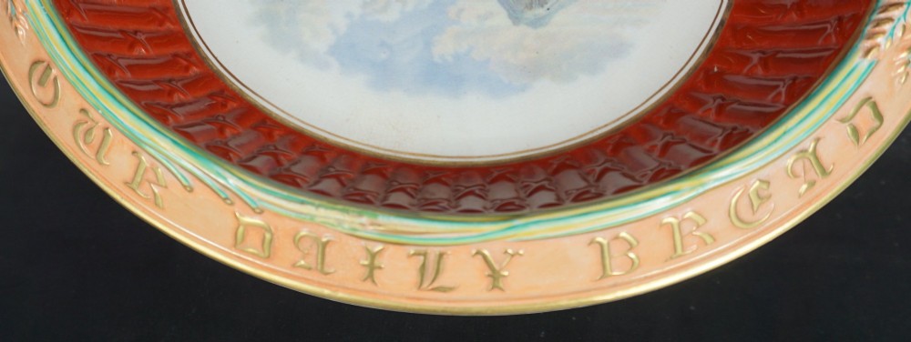 An oval Victorian ceramic bread platter featuring an embossed ochre rim with wheat motif, a red fluted inner border, and a central polychrome transfer landscape of a mountain stream. View II