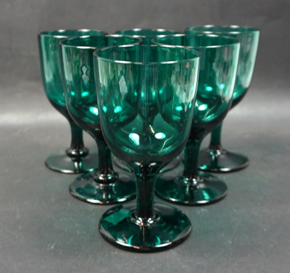 A set of six dark green Georgian blown-glass wine goblets arranged in a cluster on a grey surface.
