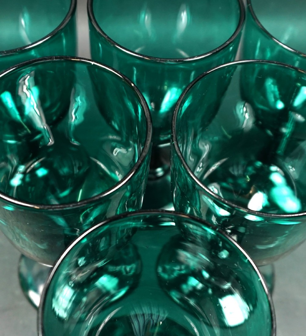 A set of six dark green Georgian blown-glass wine goblets arranged in a cluster on a grey surface. View II