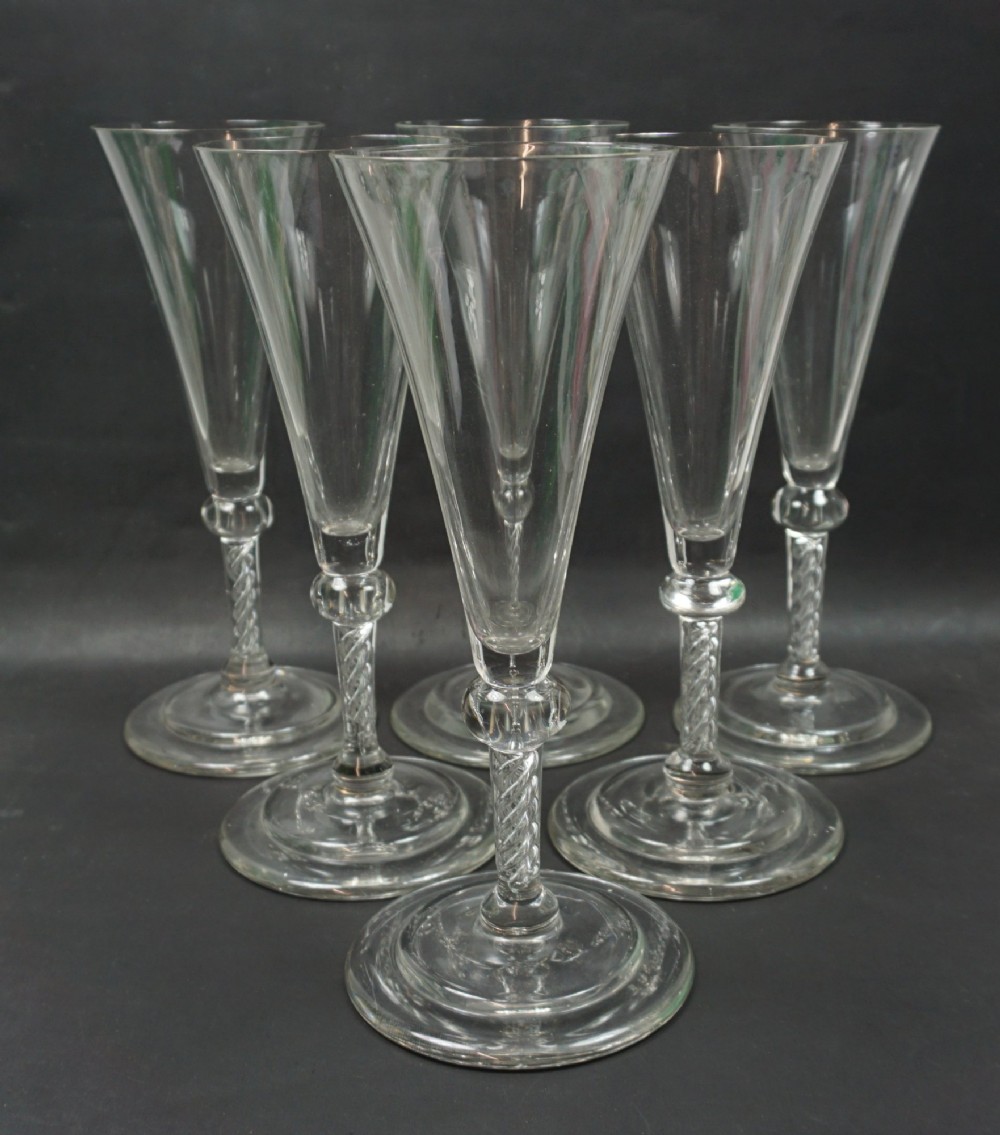 A set of six tall clear glass flutes with conical bowls, knopped air twist stems, and circular bases.
