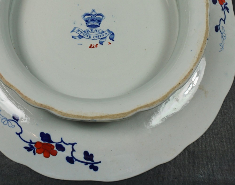 A circular ceramic plate featuring hand-coloured floral Imari patterns in cobalt blue, orange, and pink with a scalloped gilded rim. View III