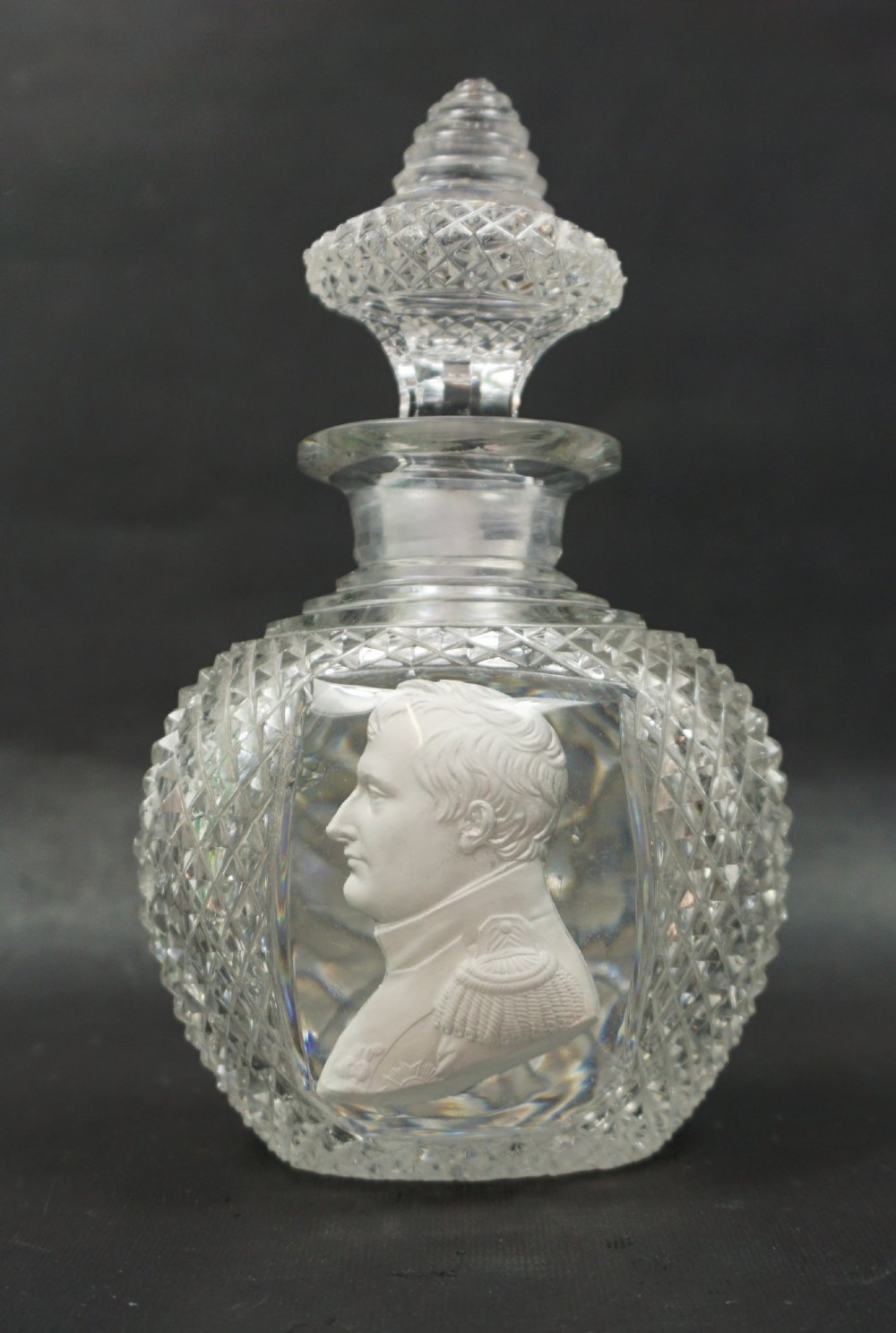 A cut clear lead crystal scent bottle featuring an embedded white ceramic sulphide profile portrait of Napoleon within a smooth oval panel, fitted with a diamond-faceted glass stopper.