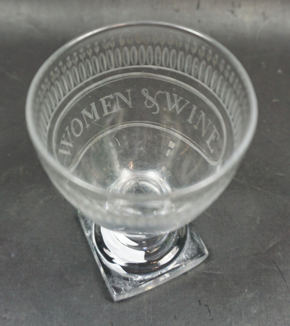 A clear Georgian glass rummer featuring a square foot, turned stem, and an engraved bowl inscribed with the words Women and Wine beneath a decorative rim band. View II