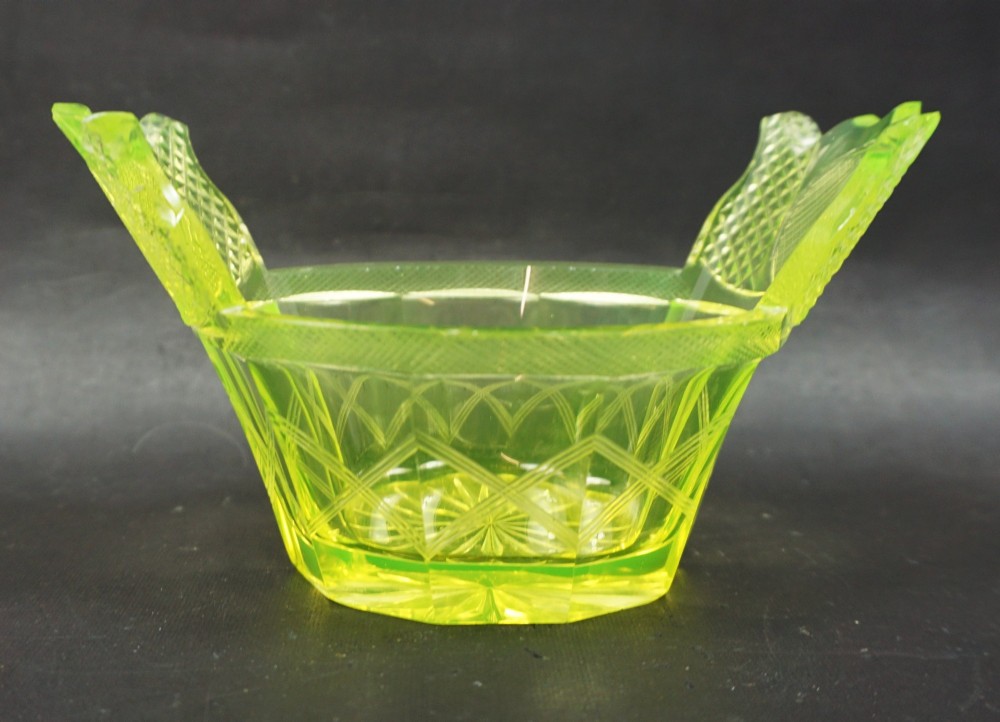 A nineteenth-century Bohemian yellow-green uranium glass dish featuring hand-cut geometric facets, diamond cross-hatching, and two flared wing-like handles.
