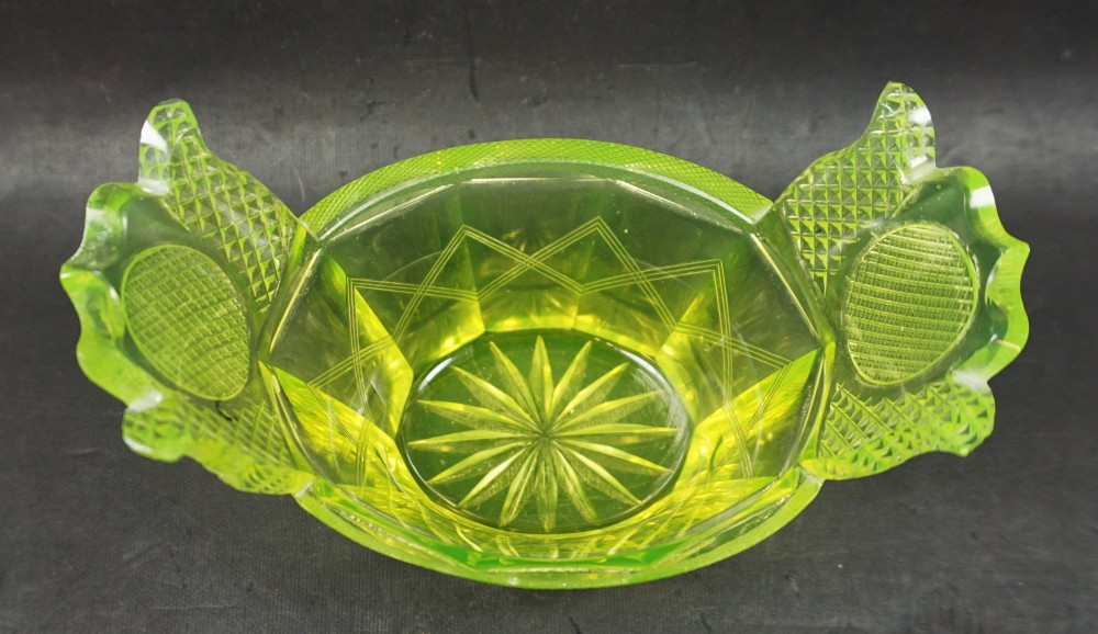 A nineteenth-century Bohemian yellow-green uranium glass dish featuring hand-cut geometric facets, diamond cross-hatching, and two flared wing-like handles. View II