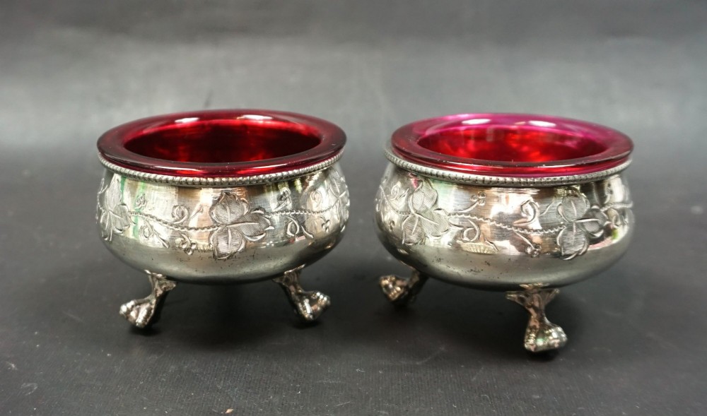 A pair of Victorian silver-plated open salt cellars with chased ivy leaf decoration and vibrant red cranberry glass liners.