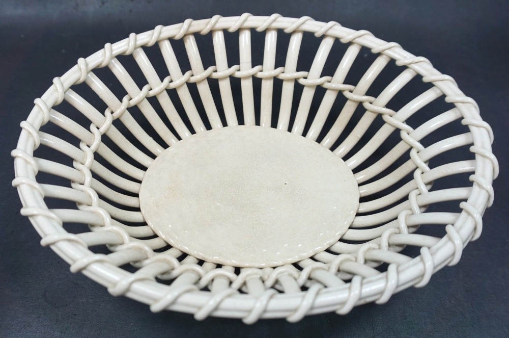 An antique creamware ceramic basket featuring openwork lattice construction imitating woven cane with a solid circular base.