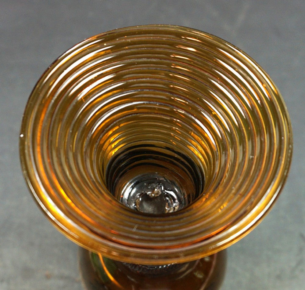 A dark amber glass roemer featuring a rounded bowl, a prunted stem, and a ribbed coiled glass foot. View II