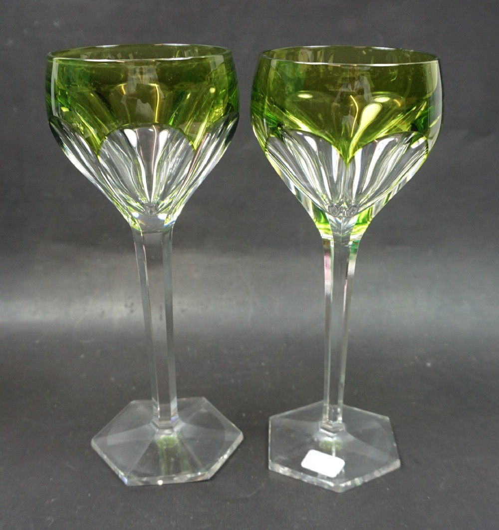 A pair of Art Deco lead crystal hock glasses featuring emerald green cased bowls with cut-to-clear facets, tall stems, and hexagonal bases.